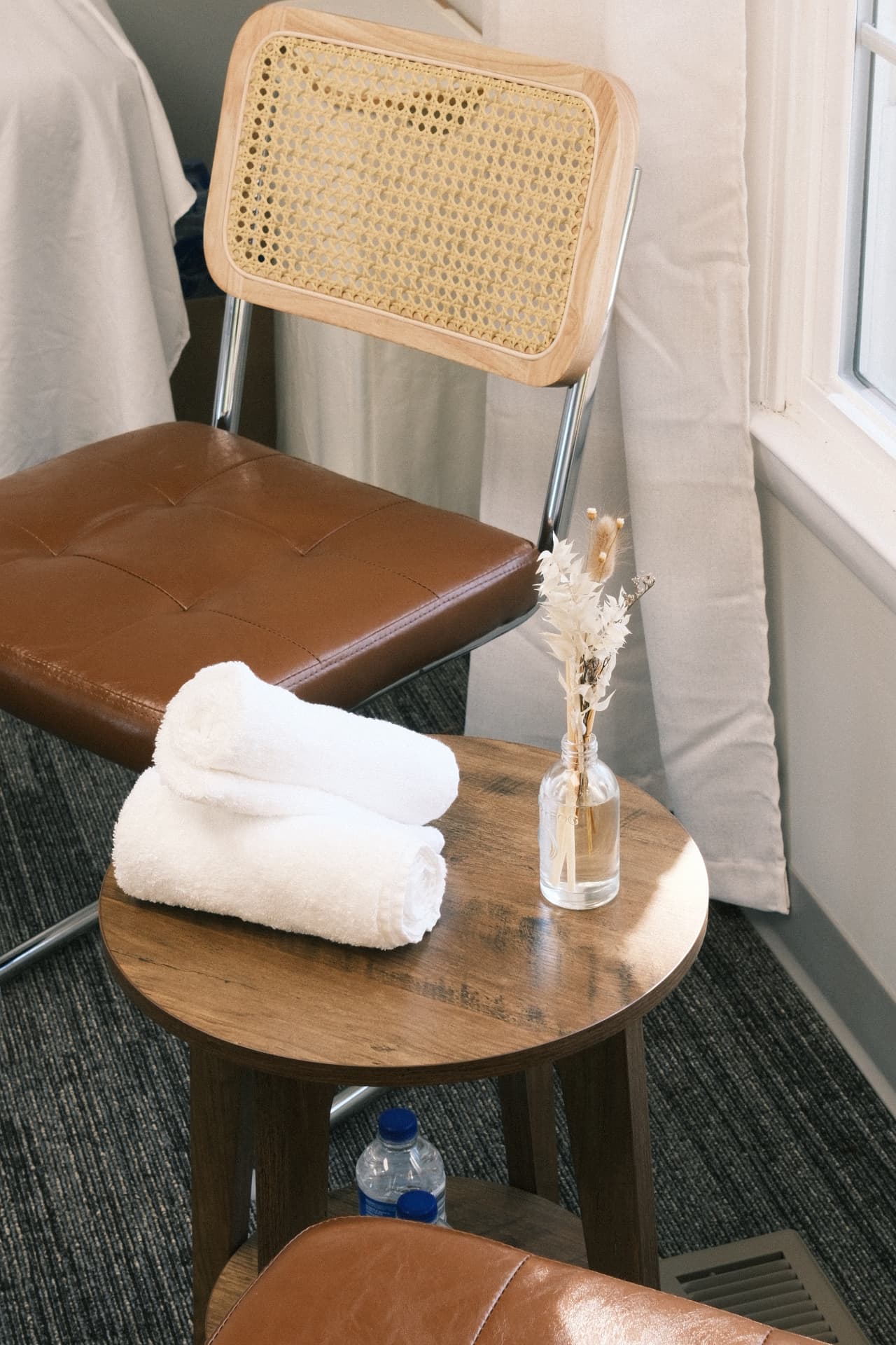 Rolled white towels, water and dried florals on a small wooden table beside the studio window