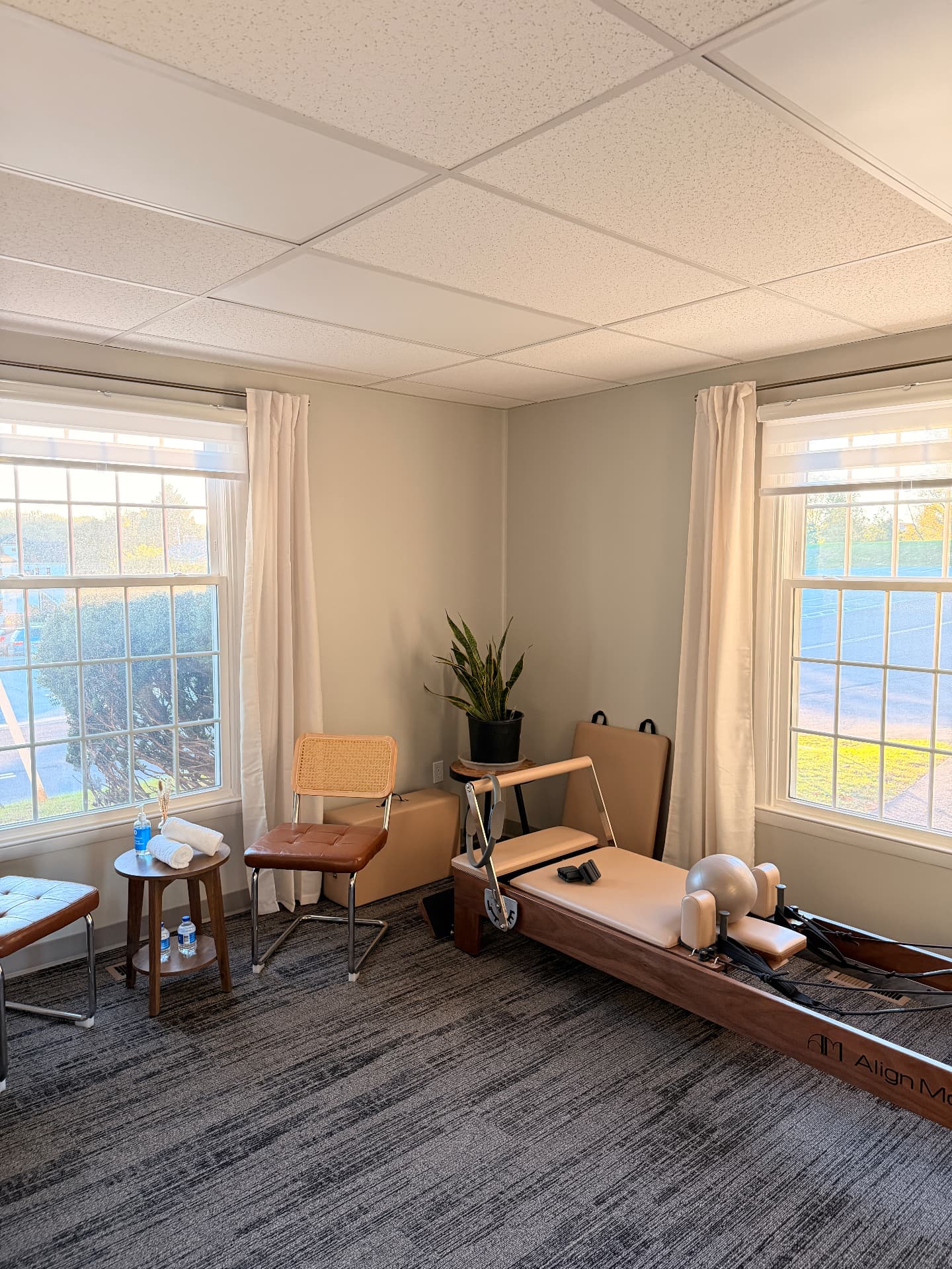 The Third Space Wellness studio: a walnut reformer with iced-coffee leather, a treatment table, and rattan chairs in the sunlight