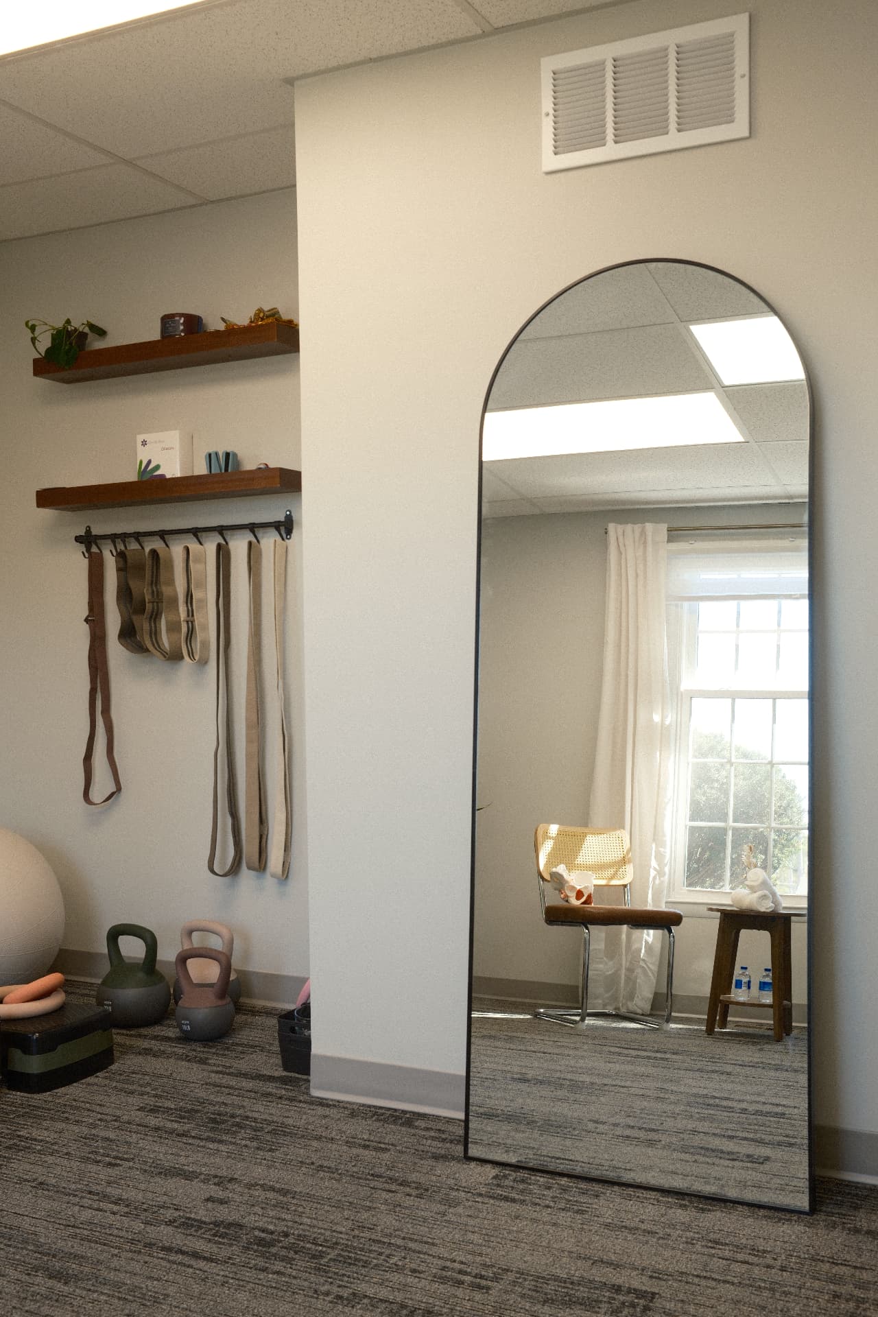 An arched floor mirror beside a wall of hanging therapy straps, shelves and light weights